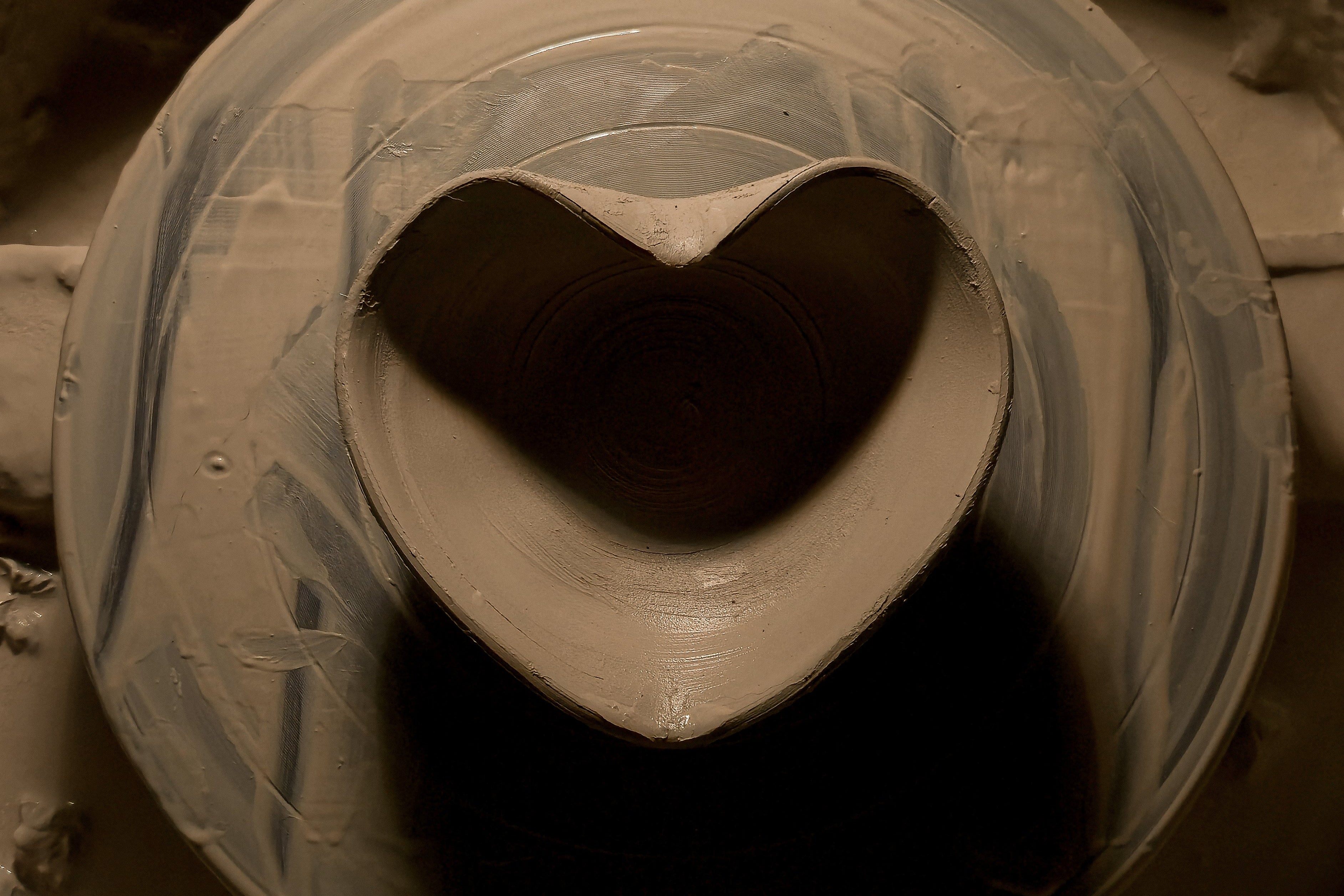 Close-up of a pottery wheel with a heart shaped bowl made of clay in a dimly lit studio