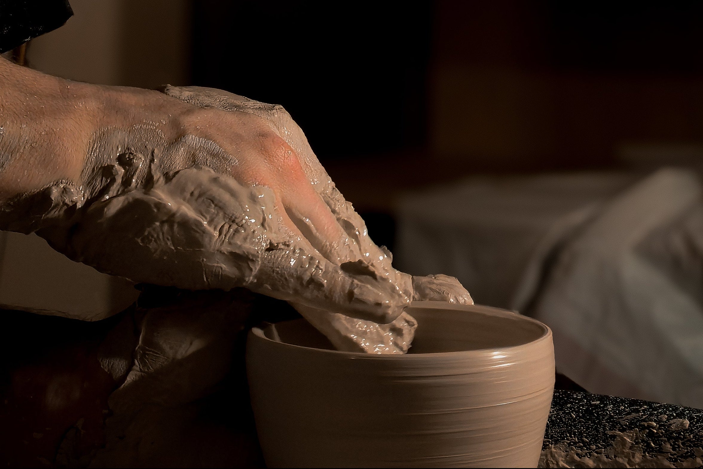 Person working with clay on a pottery wheel in a dimly lit studio.